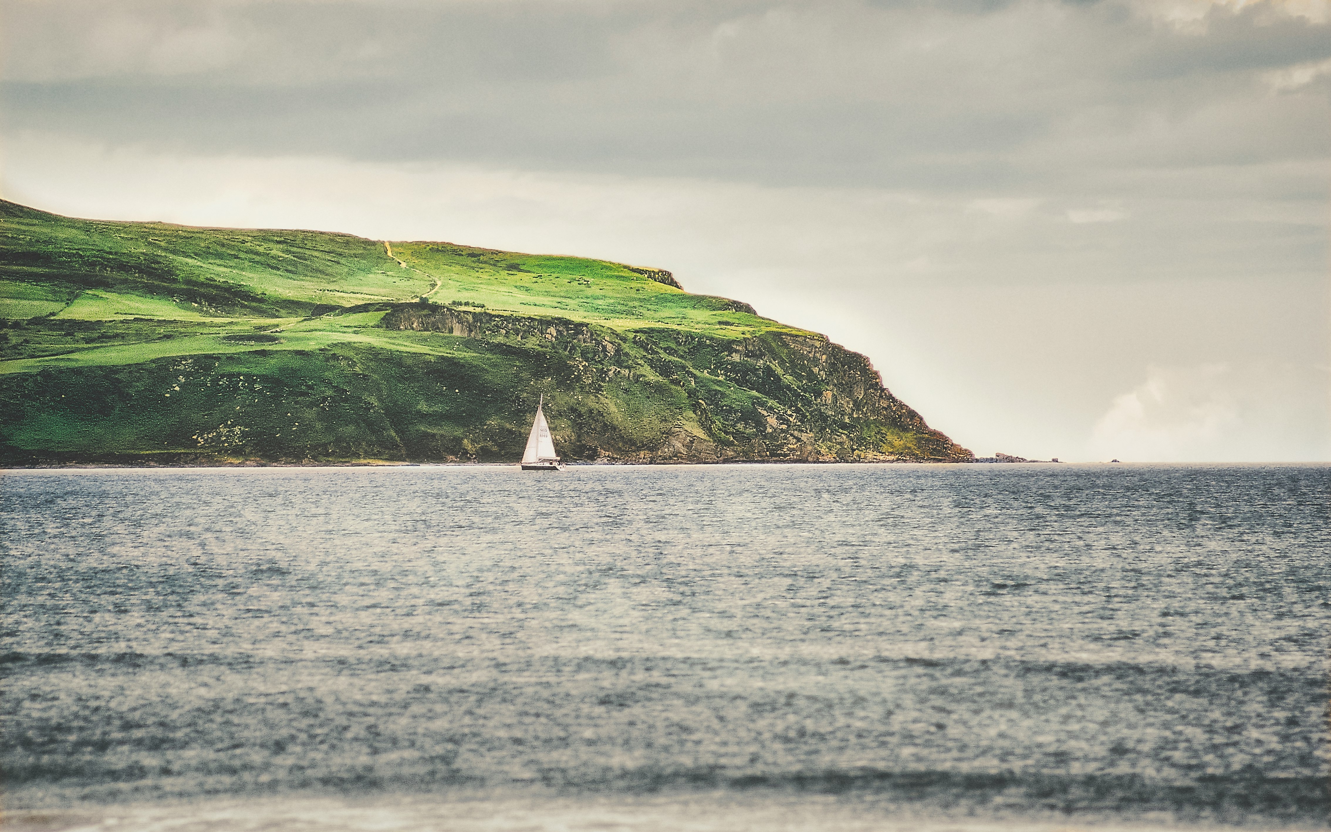 white sailboat on sea near green mountain under white clouds during daytime